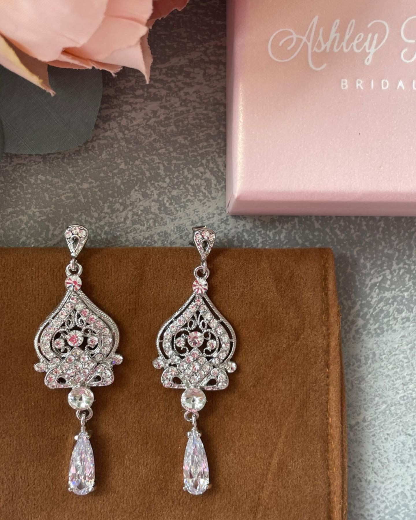 A pair of earrings sitting next to a pink box that says ashley bride