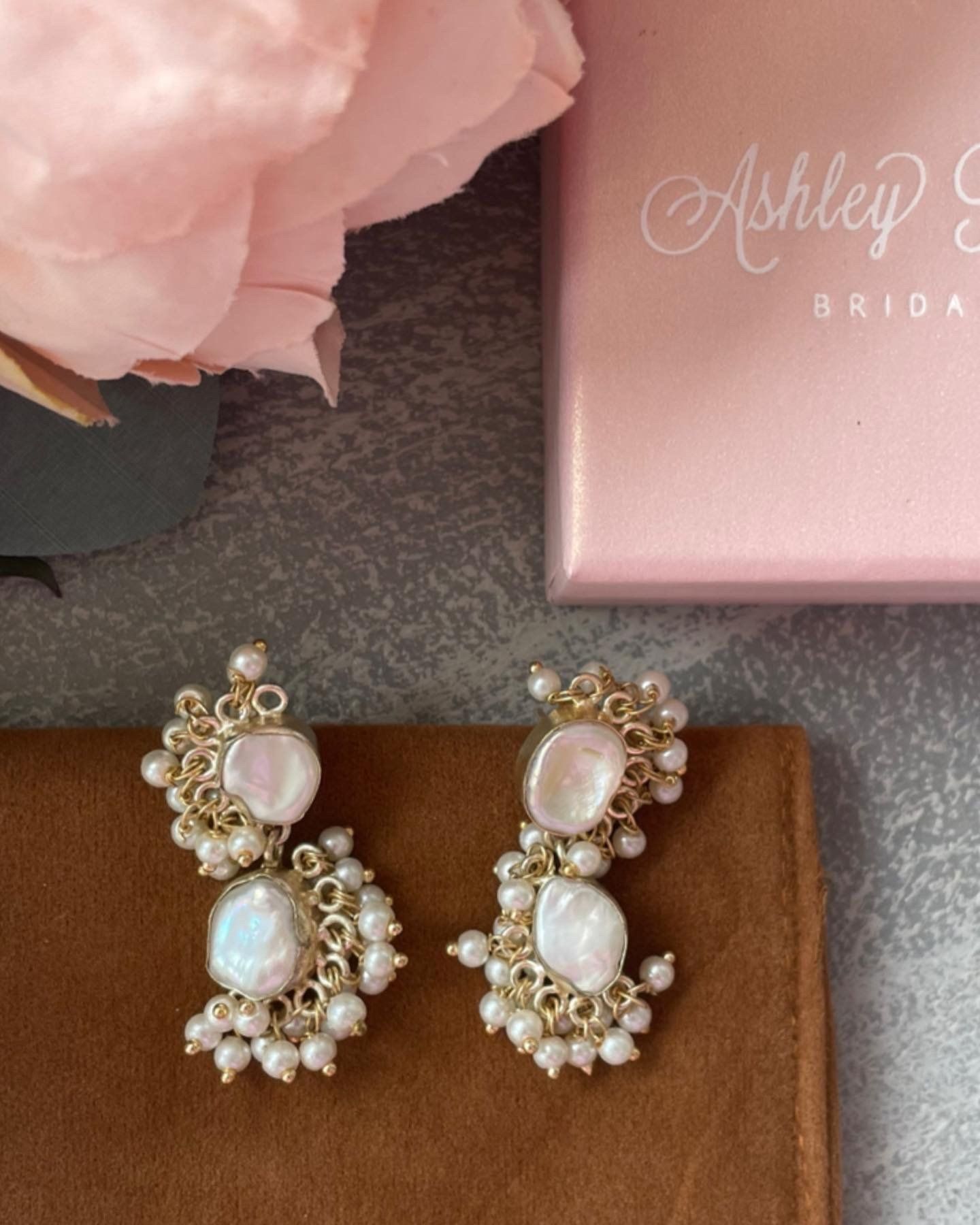 A pair of earrings are sitting next to a pink box that says ashley bride