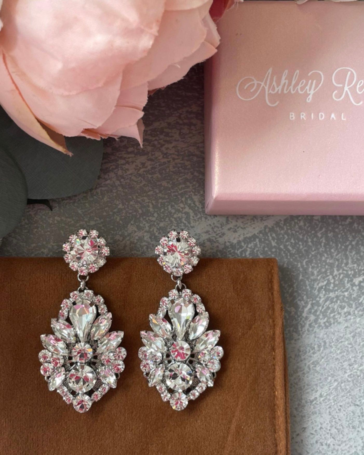 A pair of earrings sitting next to a pink box that says ashley bridal