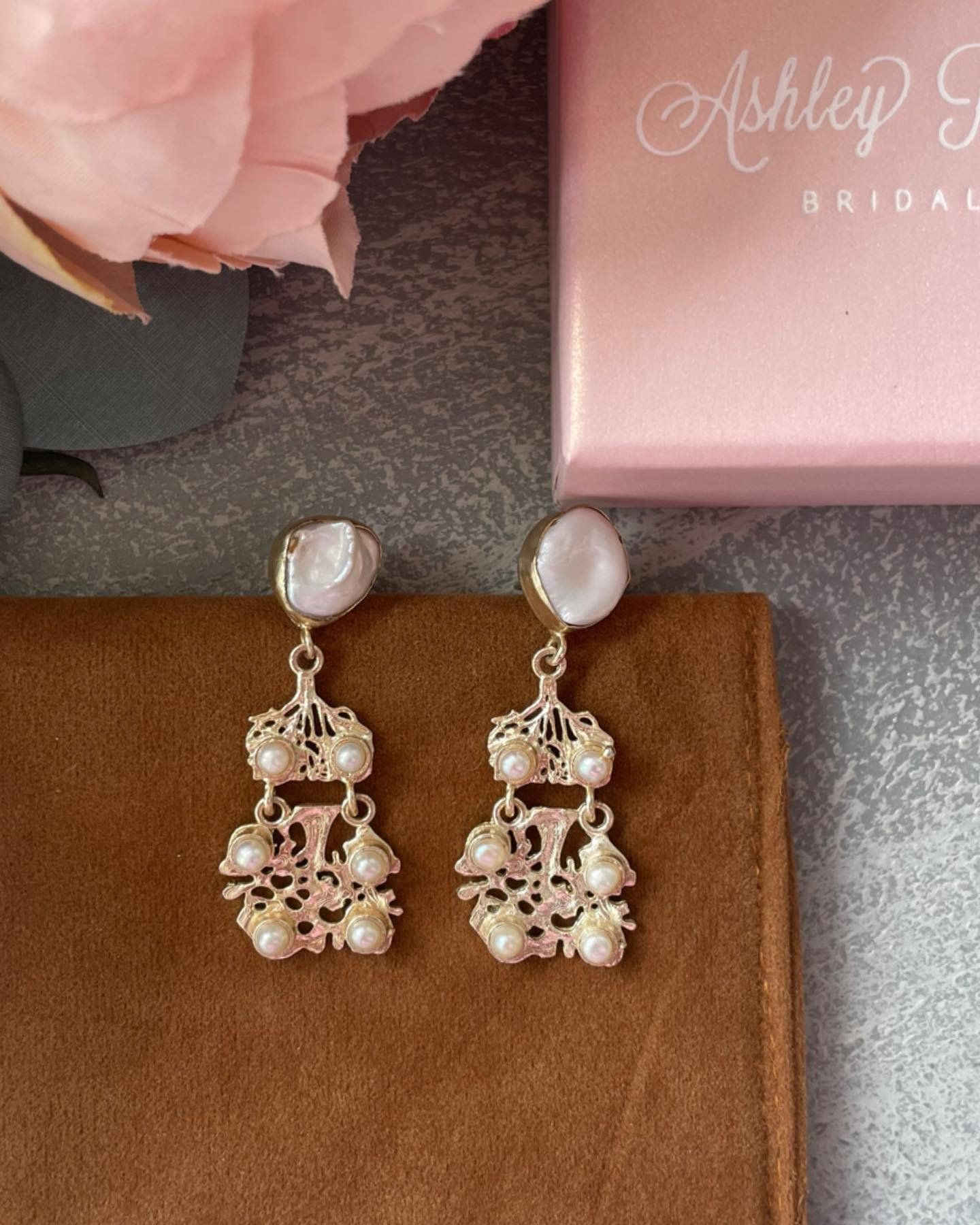 A pair of earrings sitting next to a pink box that says ashley bride
