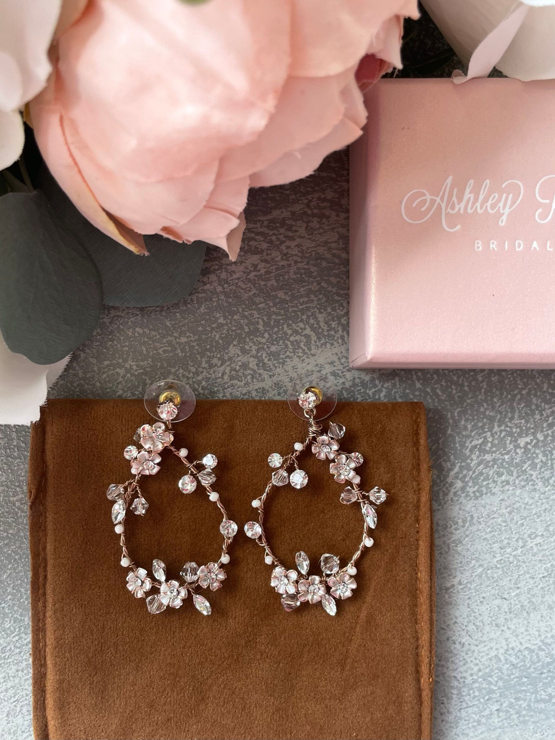 A pair of earrings sitting next to a pink box that says ashley