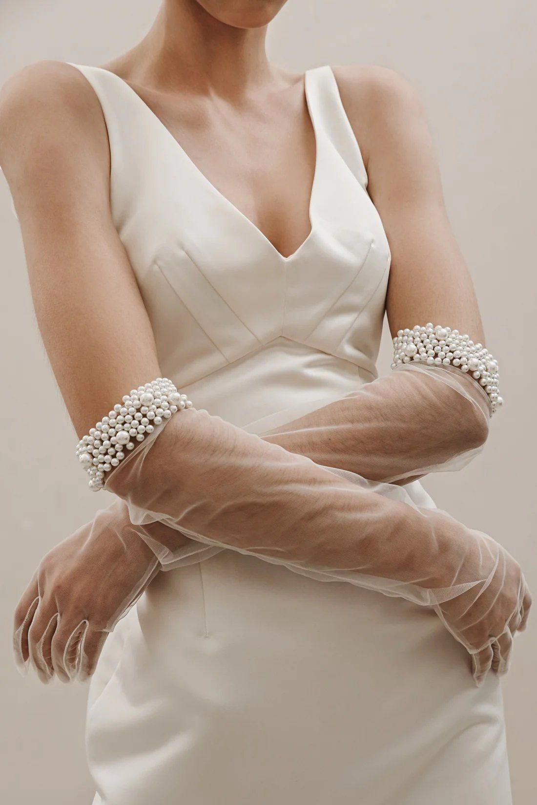 A woman in a white dress is wearing long gloves with pearls on them.