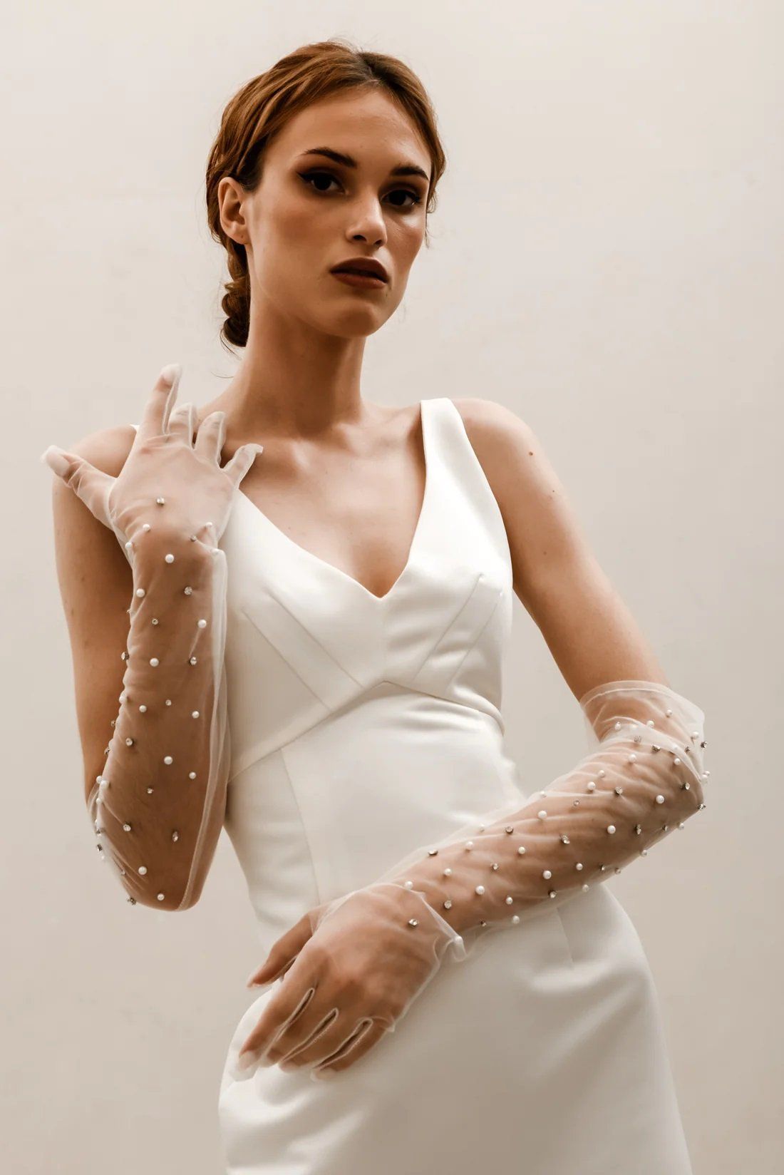 A woman in a white dress is wearing long gloves with pearls on them.