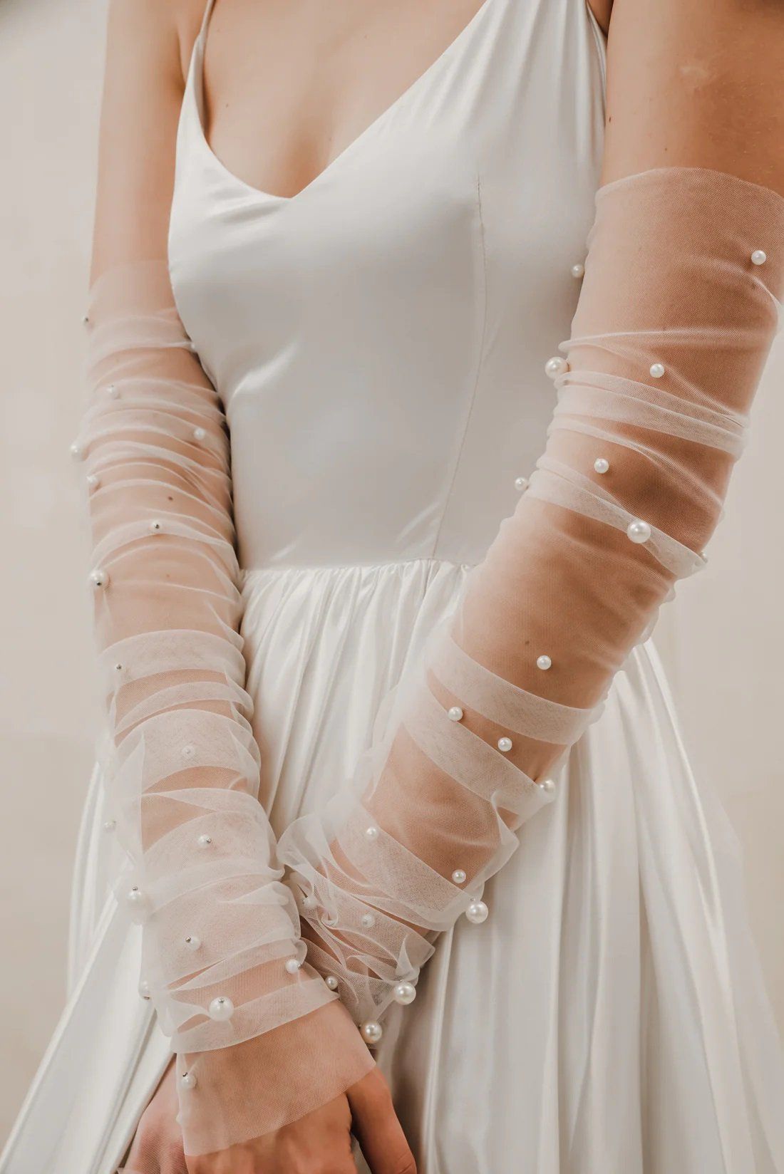 A woman in a white dress is wearing long tulle gloves with pearls on the sleeves.