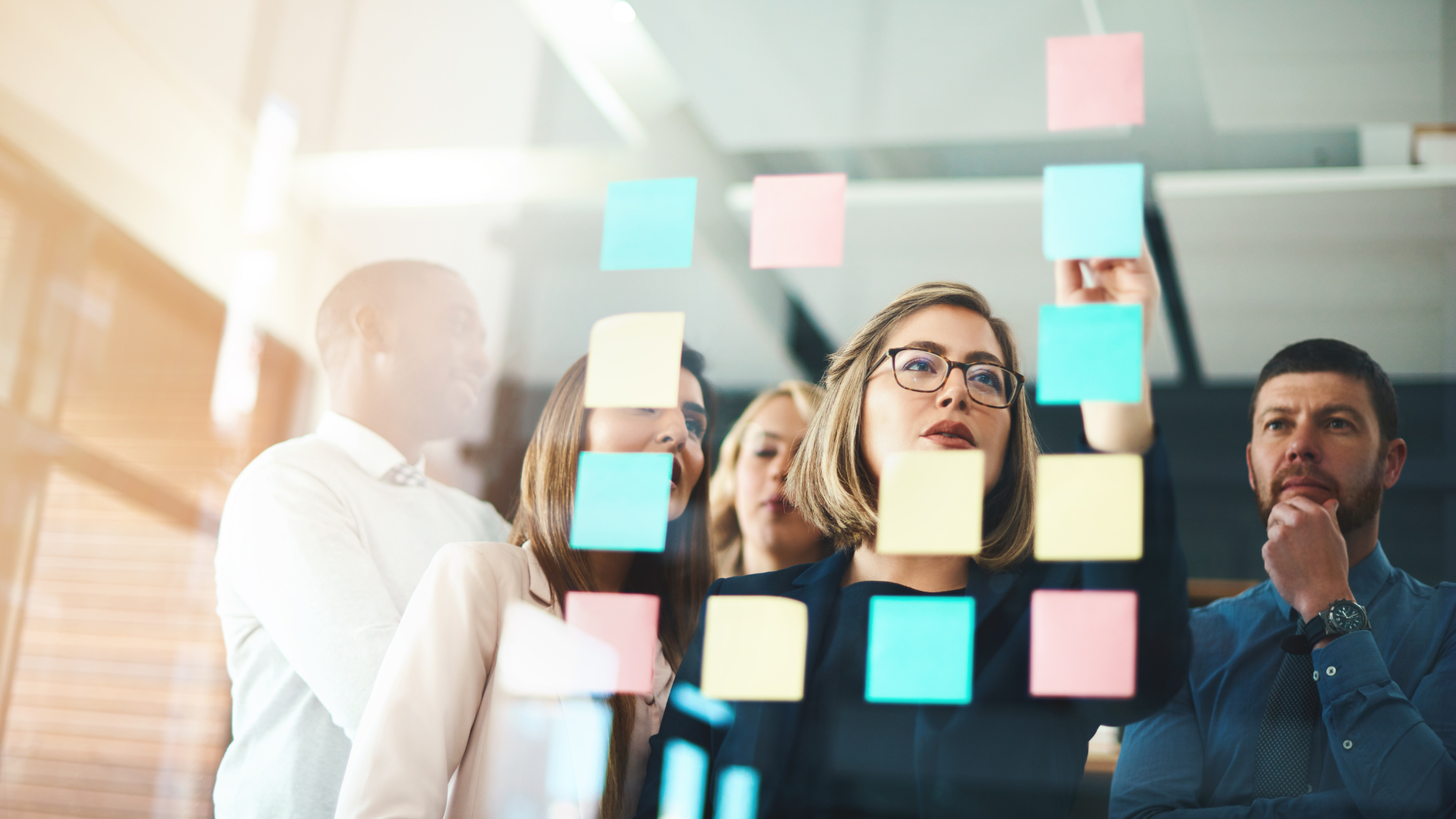 A group of people are looking at sticky notes on a glass wall.
