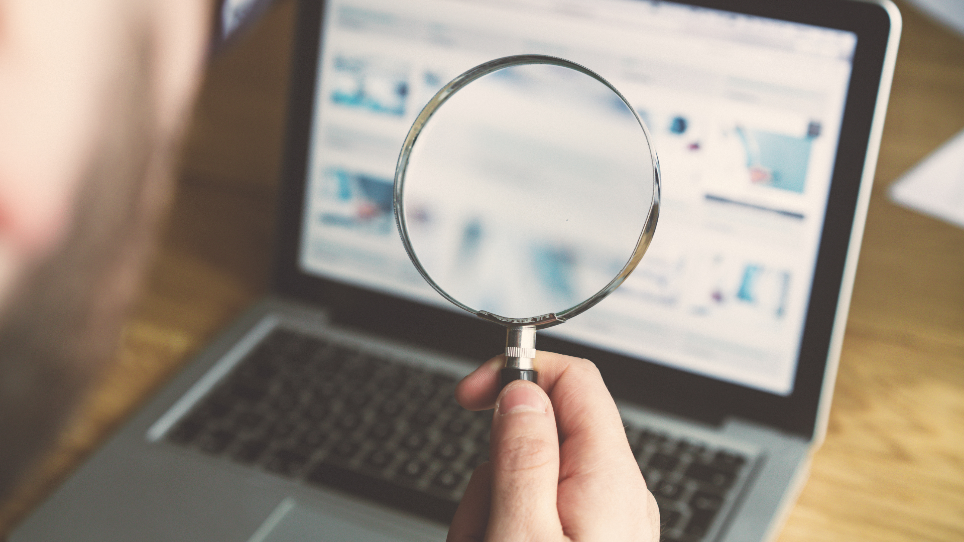 A person is holding a magnifying glass in front of a laptop computer.