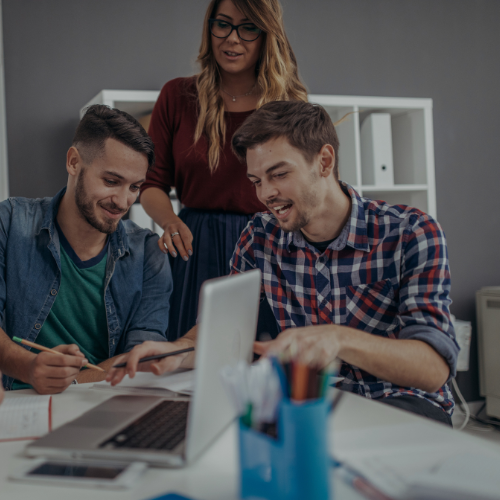 A group of people are sitting at a table looking at a laptop computer.