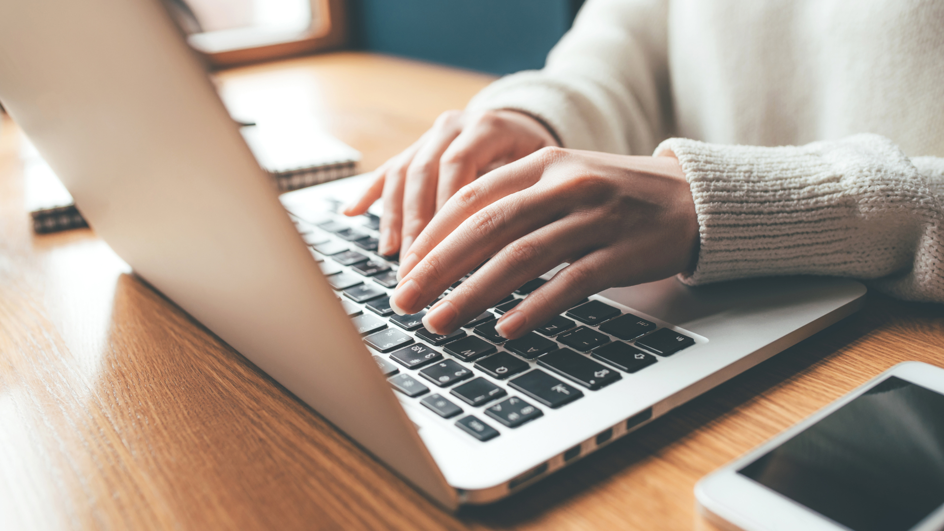 A person is typing on a laptop computer on a wooden table.