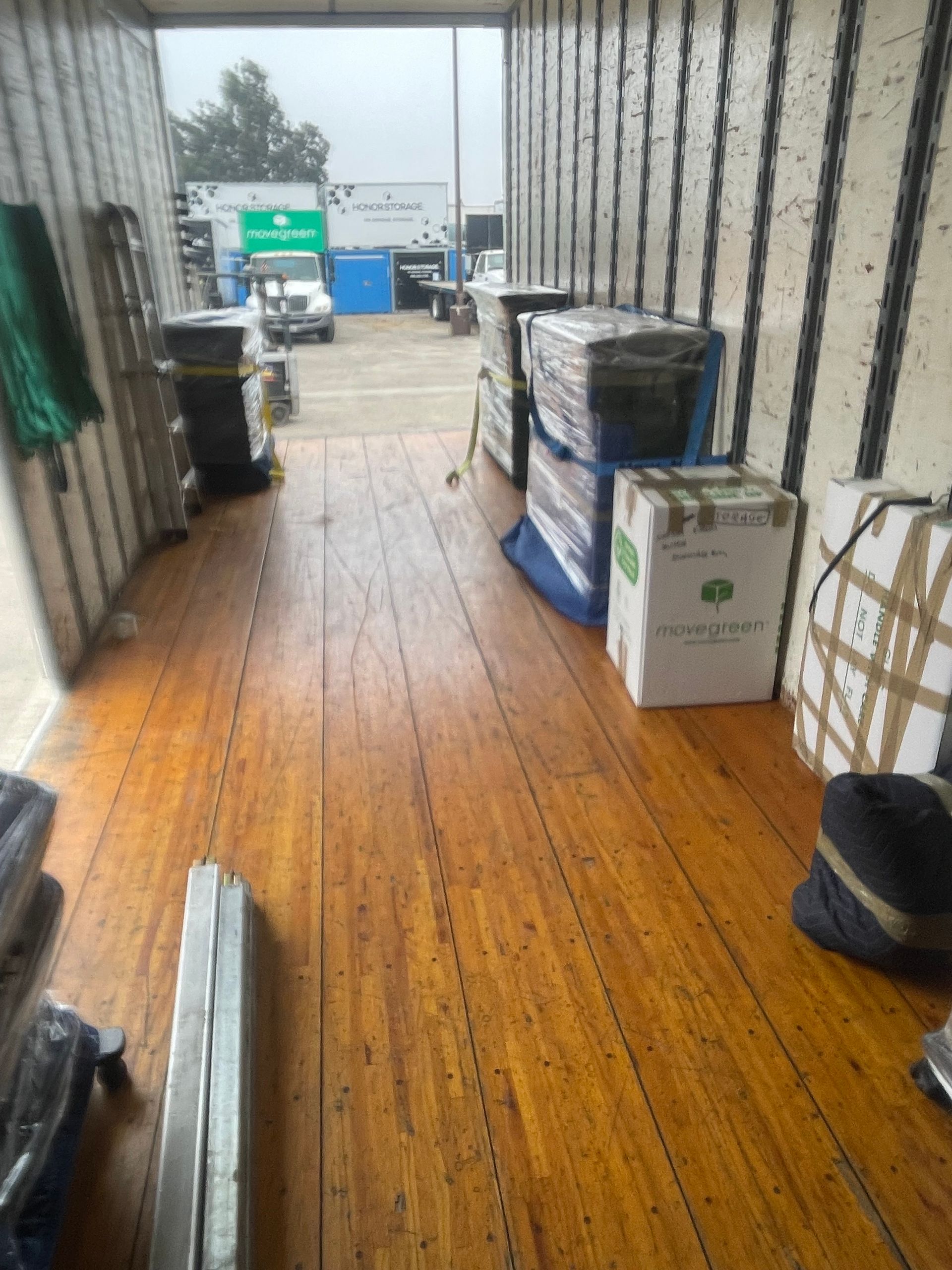 Interior of a truck bed with boxes and items, open to a view of the outside. Wooden floor.