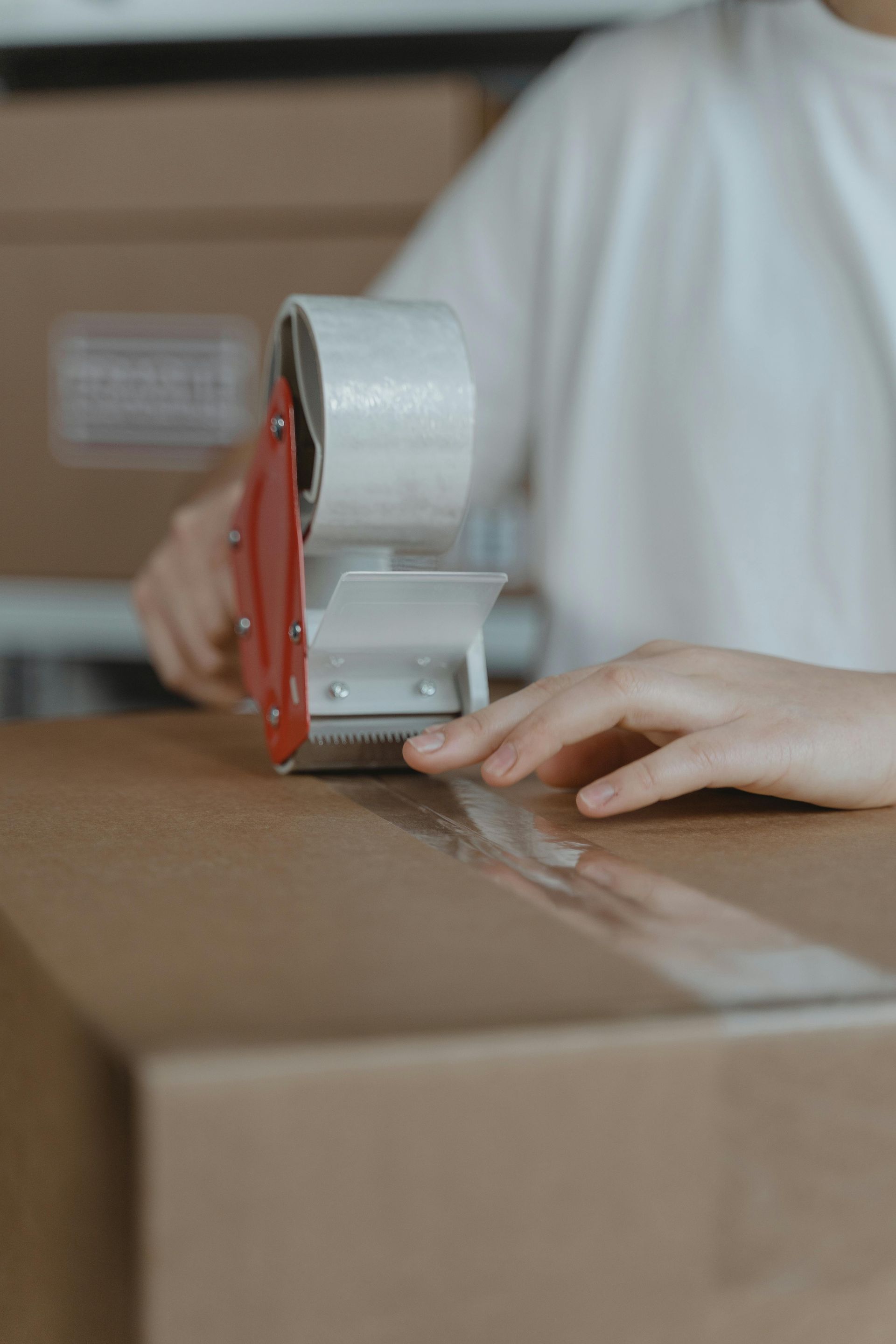 Person sealing a cardboard box with packing tape, indoors.
