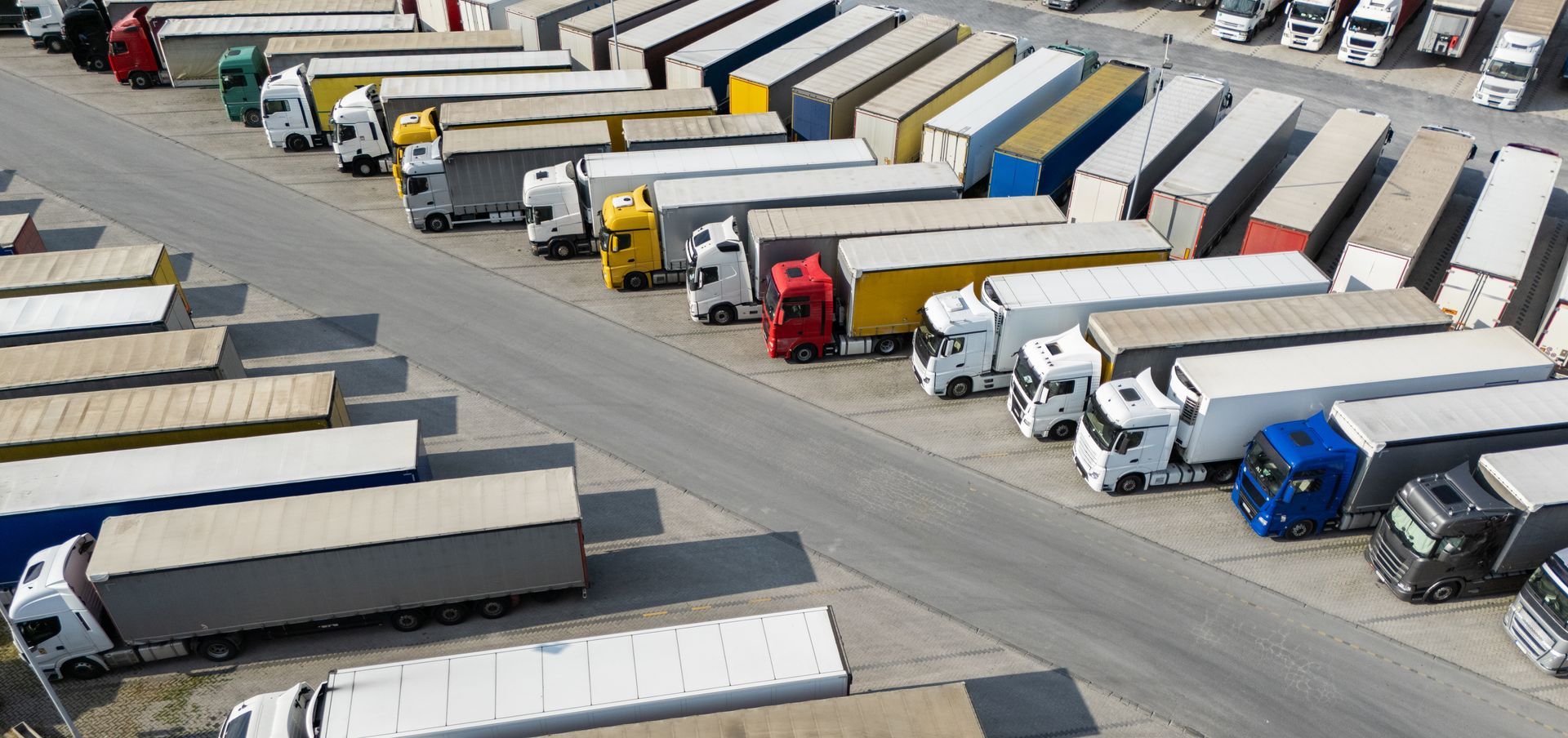 Aerial view of a truck stop filled with parked semi-trucks, mostly white and yellow cabs.