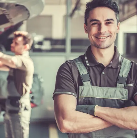 A man in overalls is smiling with his arms crossed