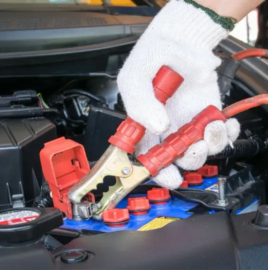 A person is charging a car battery with a pair of jumper cables