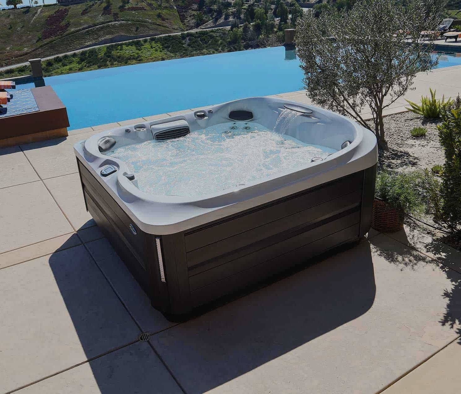 Hot tub on a patio overlooking an infinity pool and scenic vista.