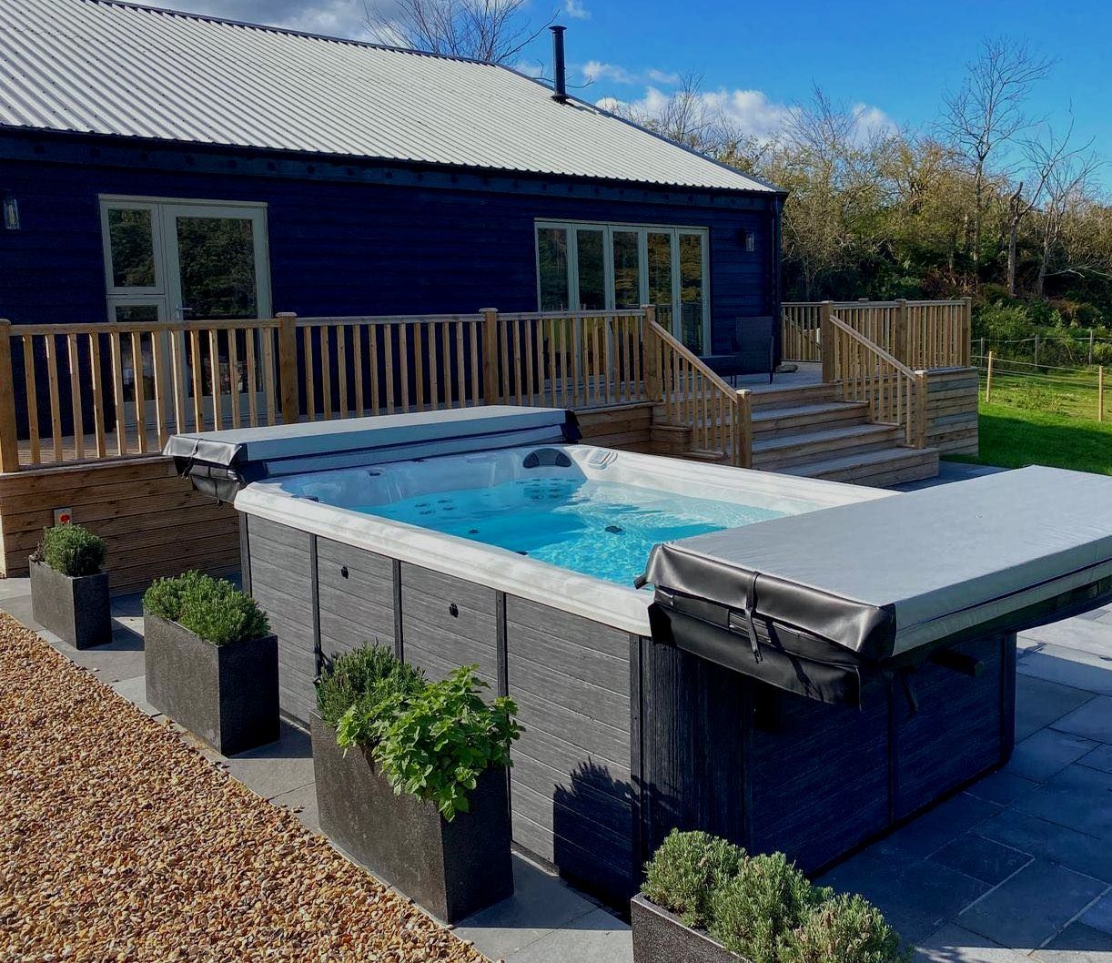 Blue cabin with a swim spa on a patio, surrounded by planters.