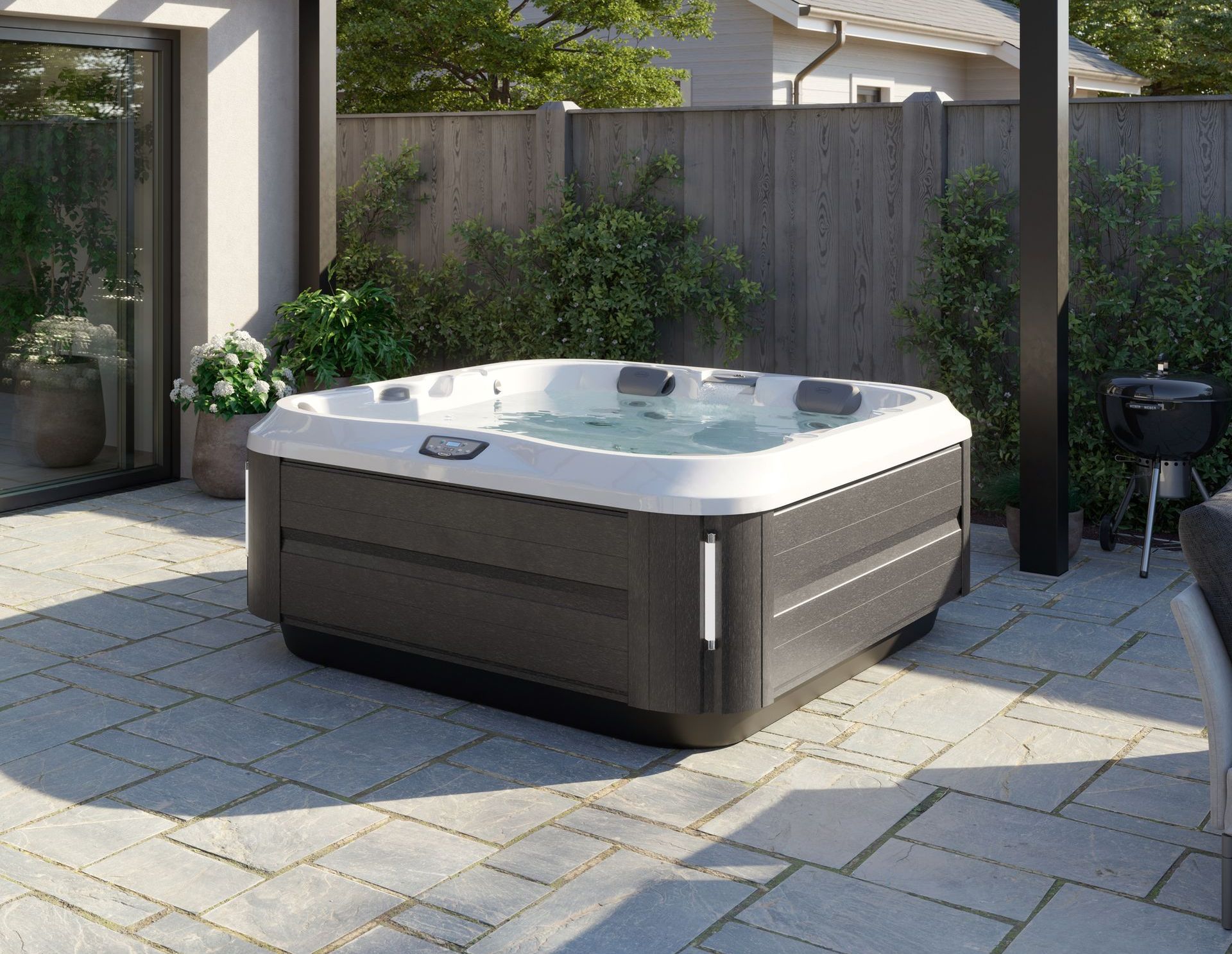 Hot tub on a patio with a dark gray exterior, surrounded by a wooden fence and greenery.