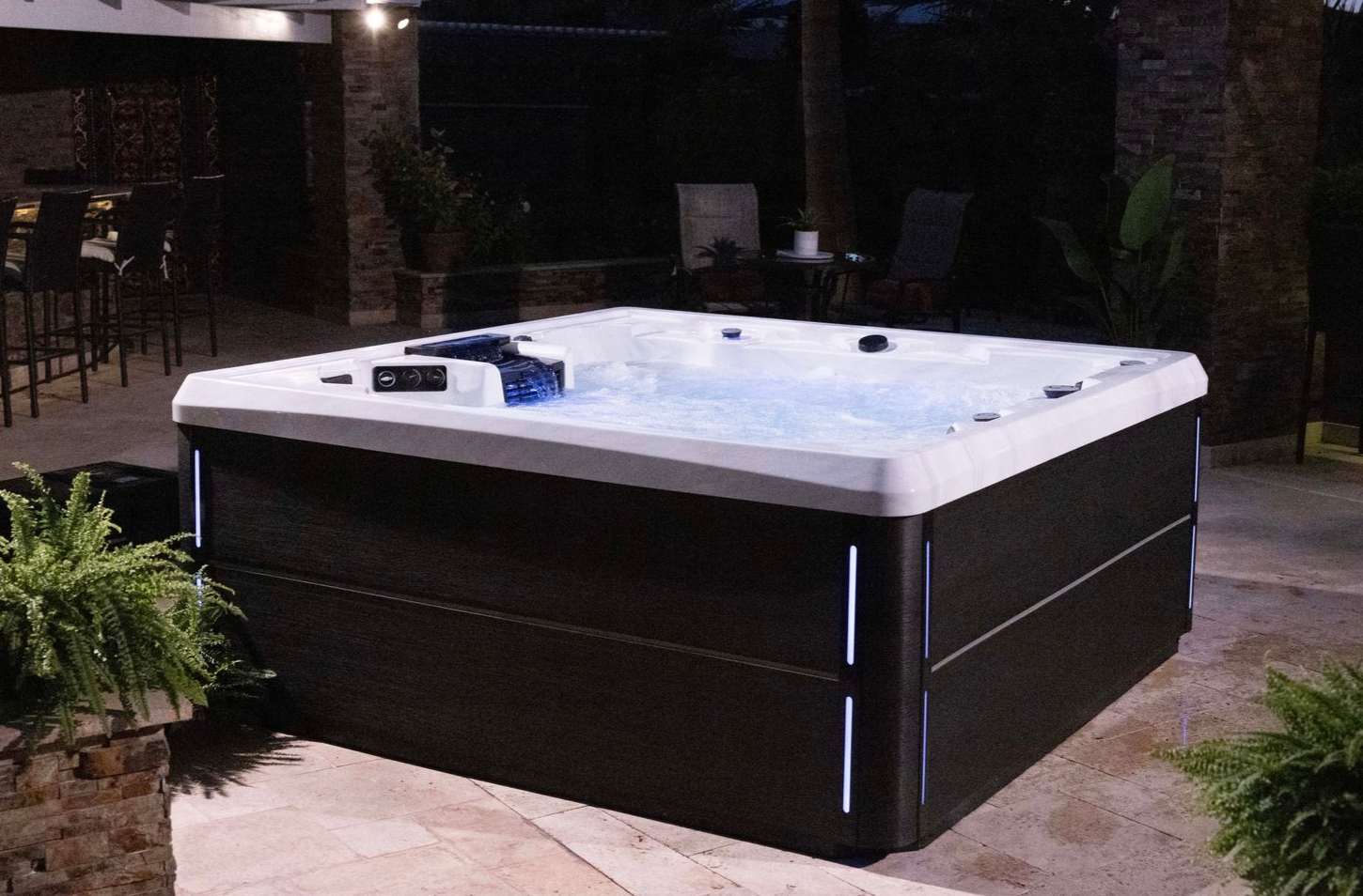 Lit-up hot tub at night with blue lights, set in a backyard patio setting.