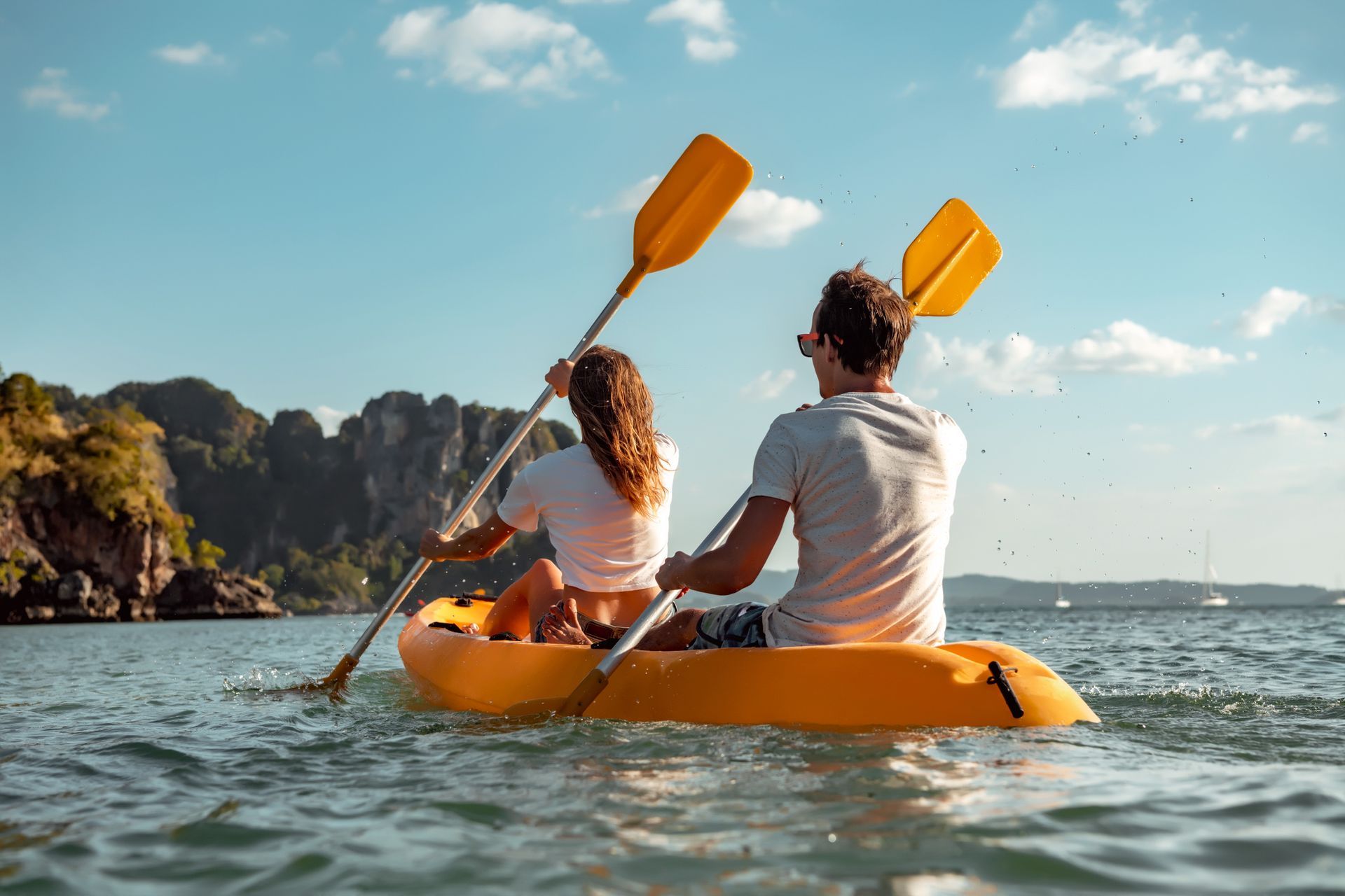 A man and a woman are paddling a yellow kayak in the ocean.