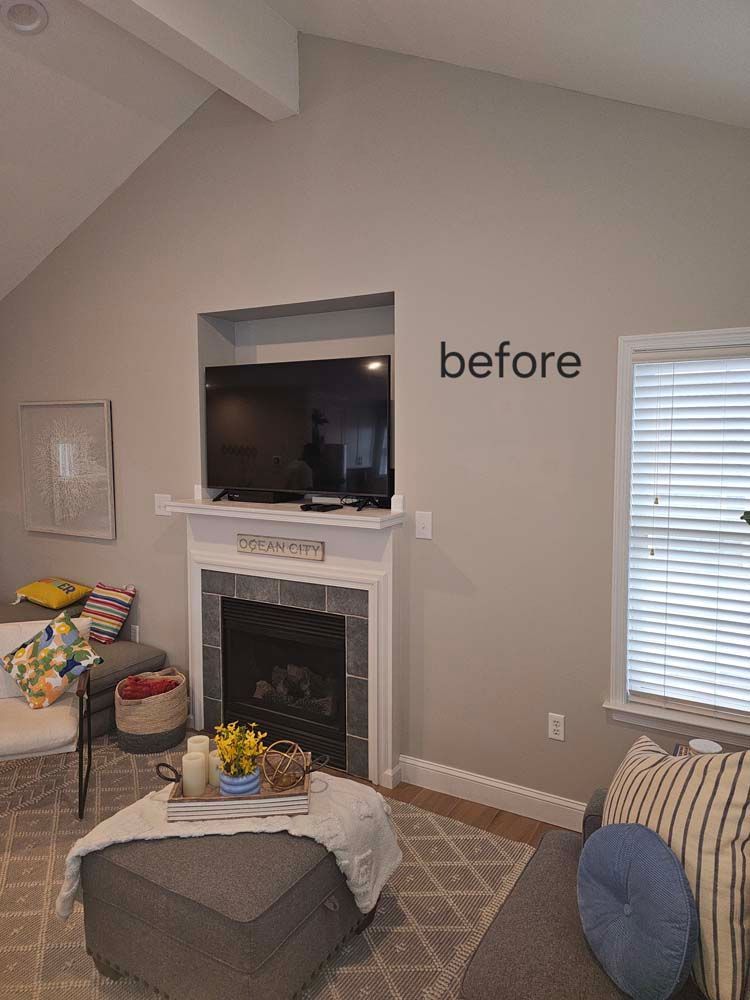 Living room with fireplace, TV, and window. Gray walls and a neutral color scheme. 