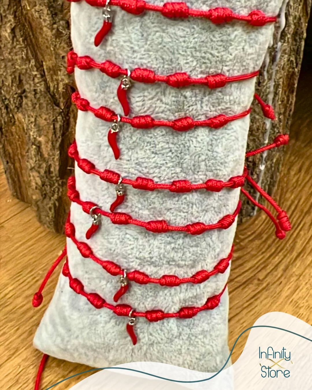 Braccialetti di corda rossa con ciondoli a forma di peperoncino su una custodia grigia, esposti su uno sfondo di legno.