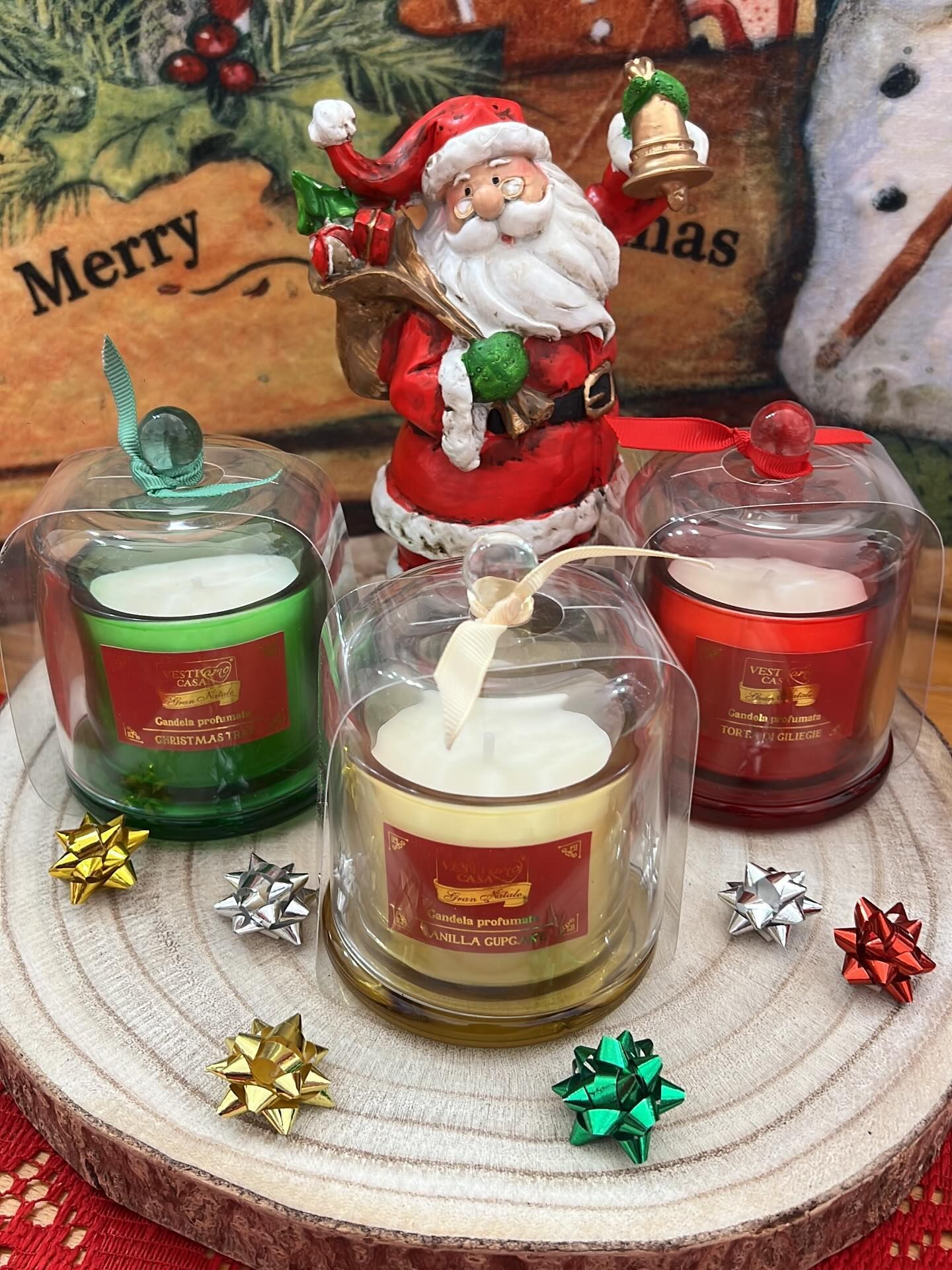 Statuina di Babbo Natale con tre candele natalizie su un sottobicchiere di legno, decorato con fiocchi.