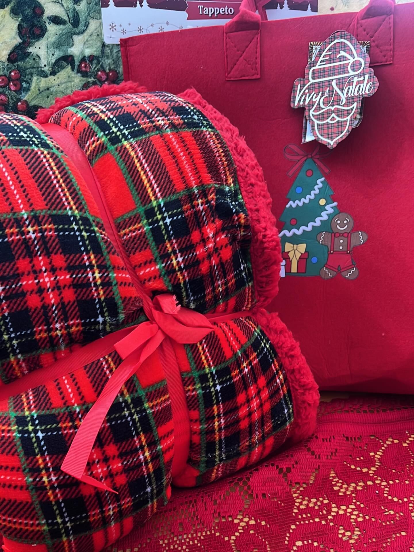 Coperta scozzese rossa legata con un nastro, accanto a una borsa rossa decorata con sagome di albero di Natale e pan di zenzero.