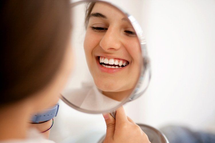 A woman is looking at her smile in a mirror.