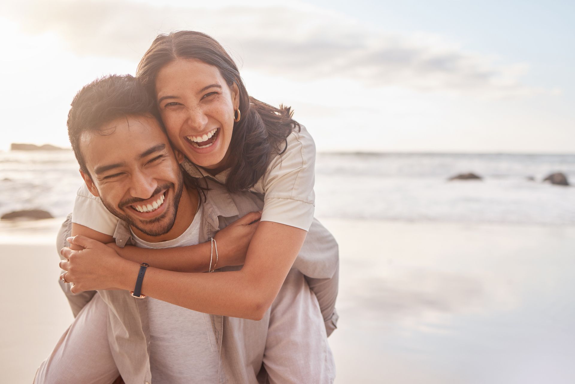 A man is carrying a woman on his back on the beach.