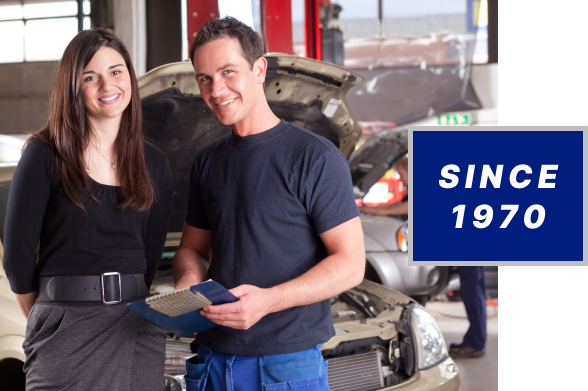 Man with clipboard, woman smiling, car in repair in background | Automotive Specialist