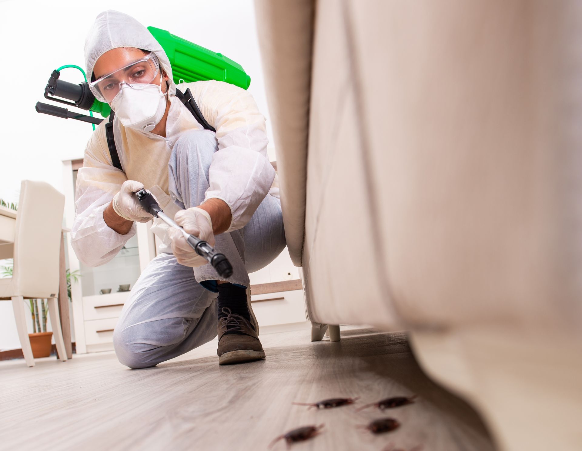 A man wearing a mask and gloves is kneeling on the floor in a living room.