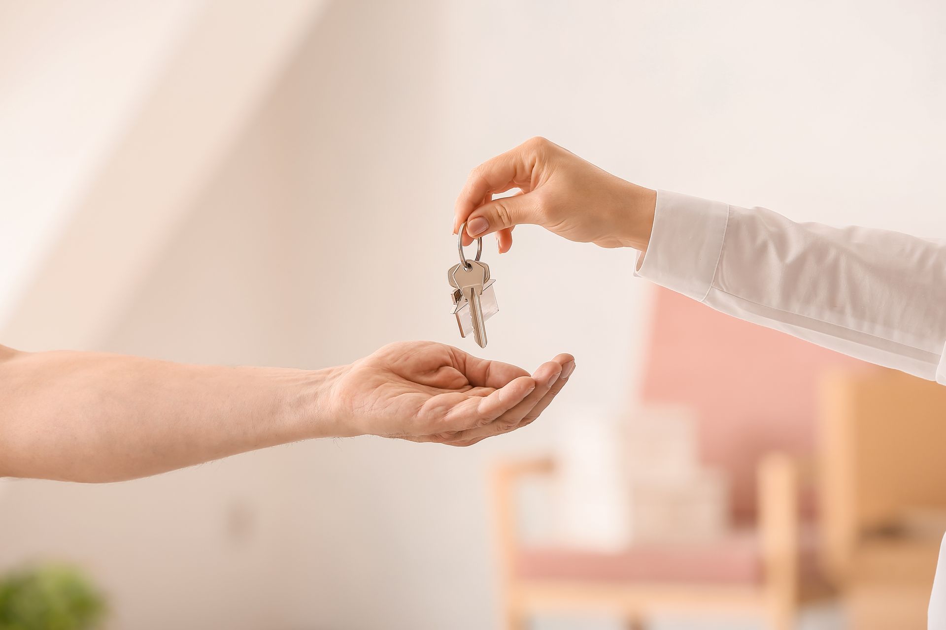 One person hands a set of keys to another person in a bright, indoor setting.