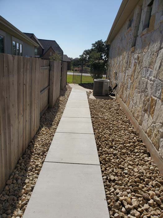 A sidewalk leading to a house with a wooden fence