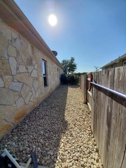 A stone house with a wooden fence and gravel in front of it.