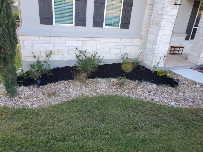 A lawn with black mulch and rocks in front of a house