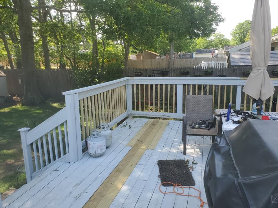 An outdoor wooden deck under construction with grey painted railings, new bare wood planks, and a grill.