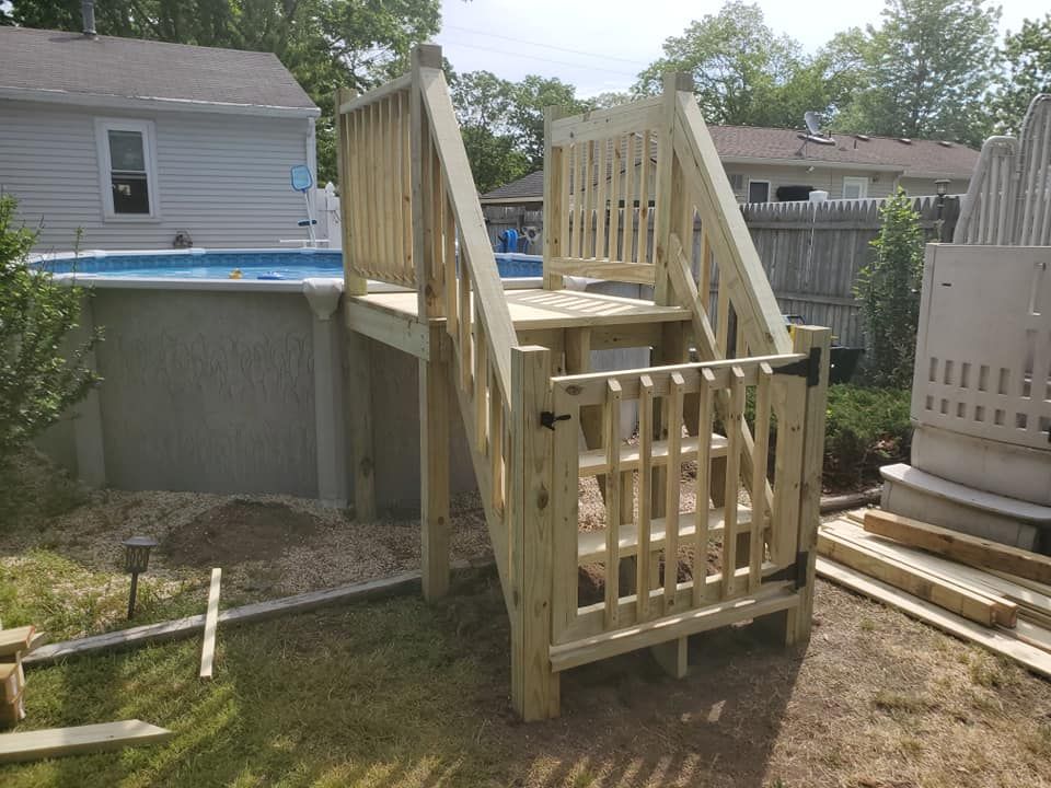 A new, light-colored wooden pool deck and stairs with a safety gate, installed next to an above-ground swimming pool.