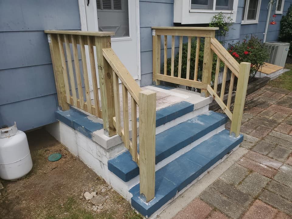 Exterior house steps with painted blue treads, a white concrete foundation, and a newly installed wooden railing.