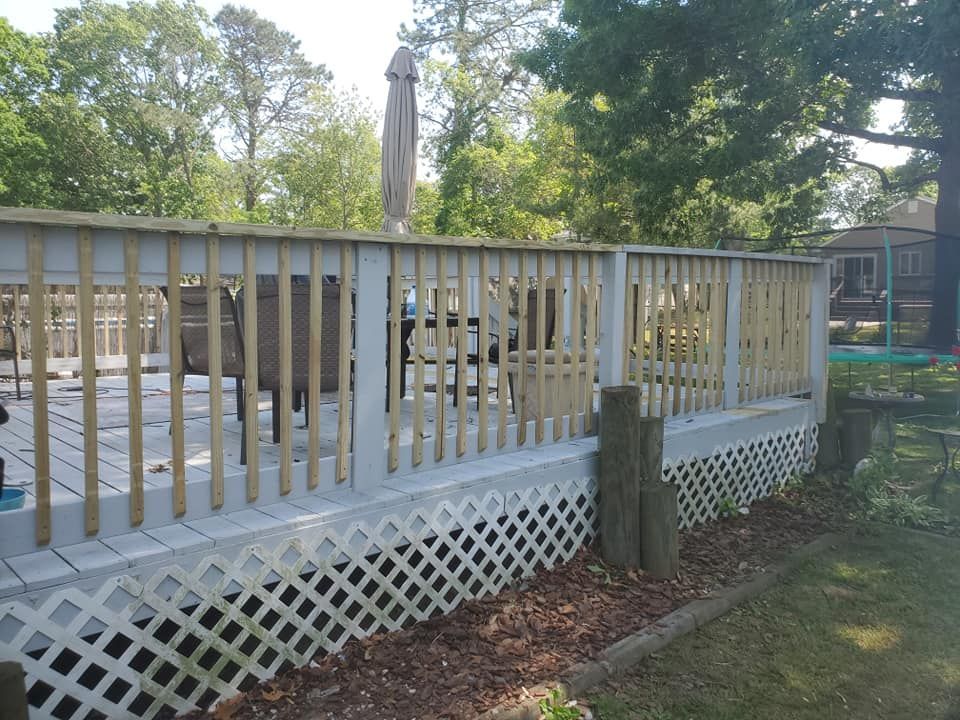 A white wooden deck with vertical balusters and lattice skirting, featuring patio furniture and an umbrella outdoors.