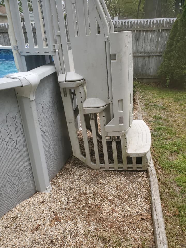 A white plastic swimming pool staircase attached to an above-ground pool, situated on wood chips in a backyard.
