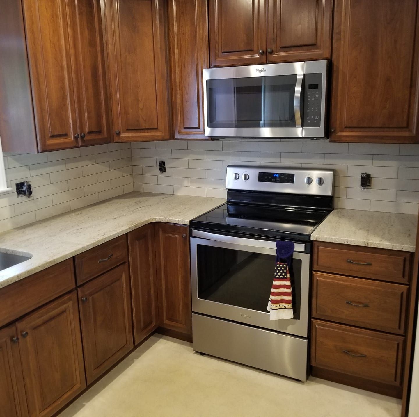 A kitchen with wooden cabinets, light countertops, a stainless steel oven, a microwave, and a white tiled backsplash.