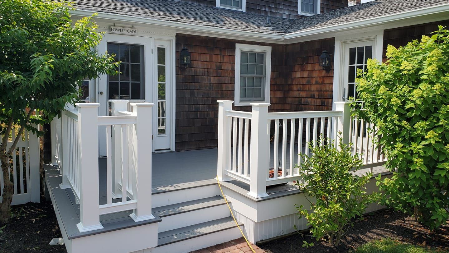 A gray wooden deck with white railings and stairs leads to the exterior of a house with brown cedar shake siding.