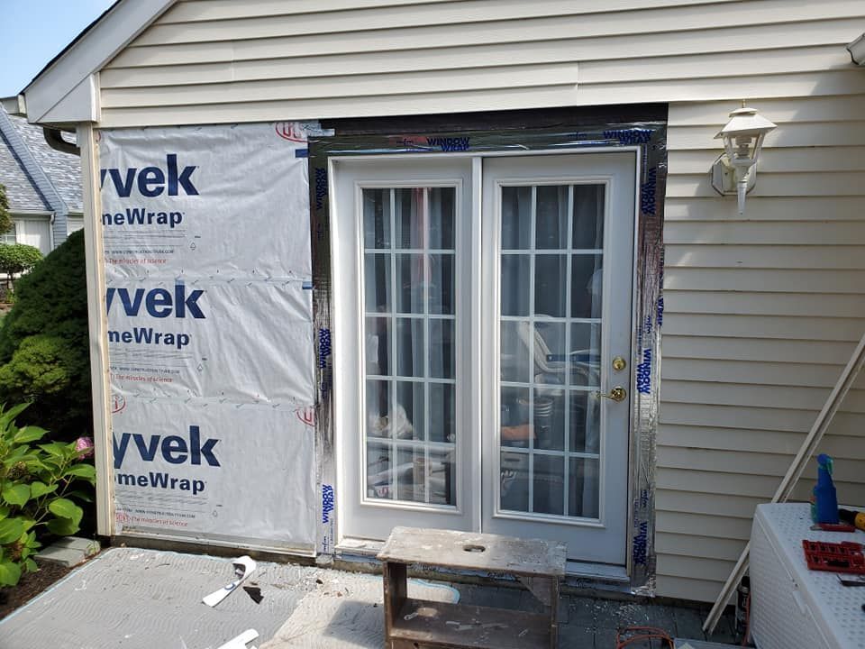 White double doors installed in a house exterior with Tyvek house wrap visible on the left and siding on the right.