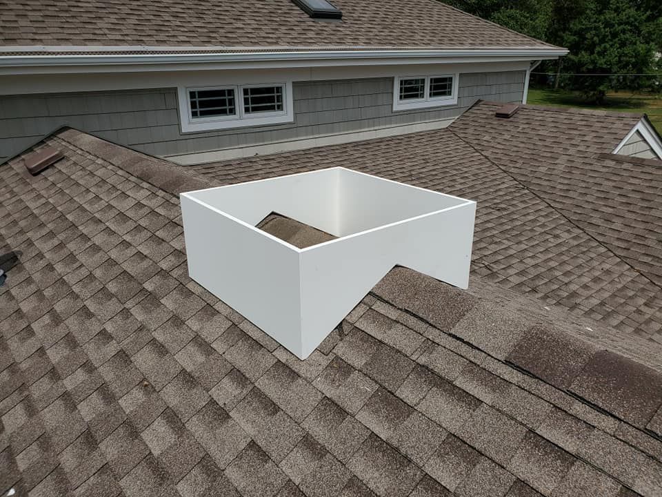A white, box-like square frame mounted on a shingled residential roof over a valley junction.