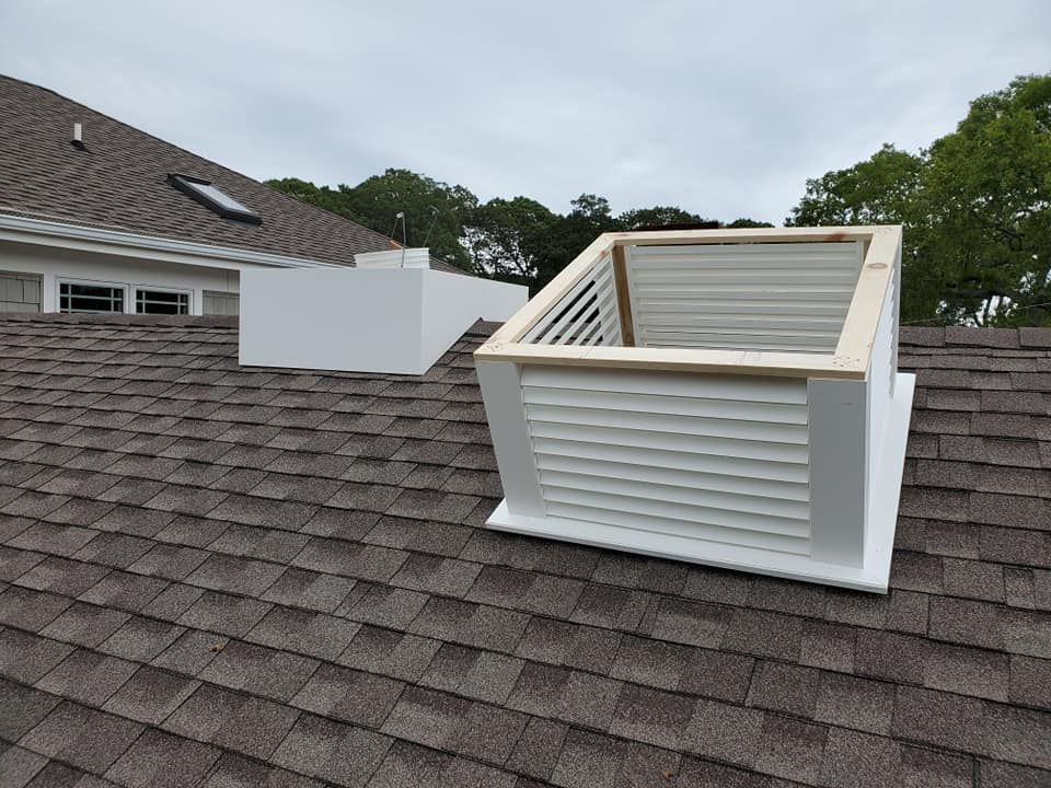 A roof with brown shingles features two white ventilation structures, one with open, slatted sides and a wooden trim top.