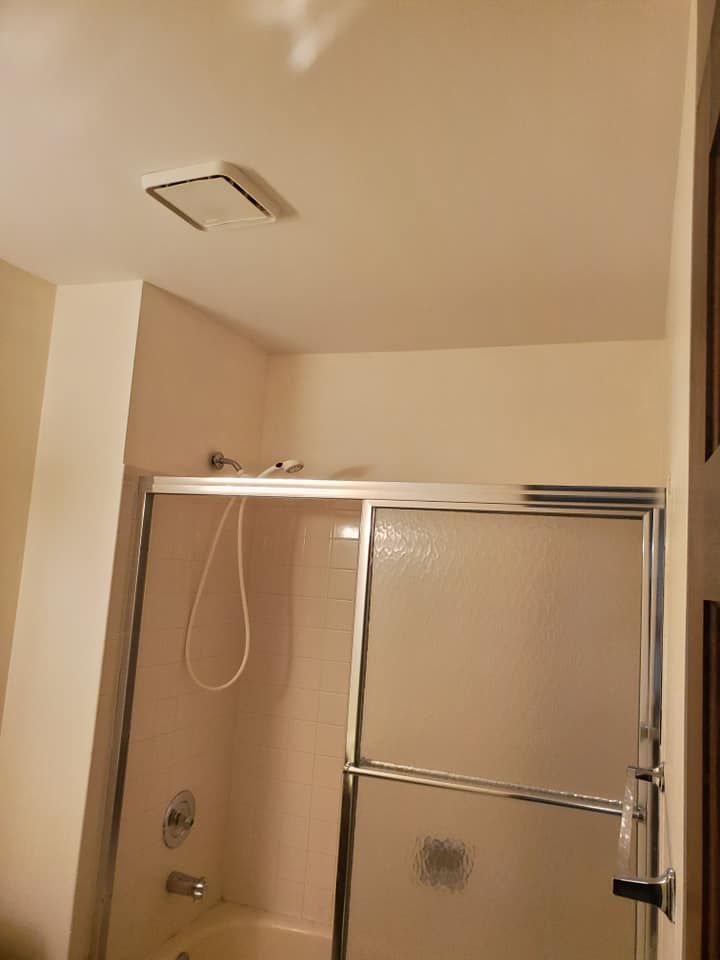 A shower stall with a sliding glass door and a wall-mounted showerhead, featuring a ceiling exhaust fan above.