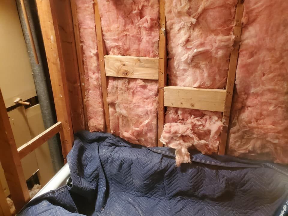 Interior wall under construction with pink fiberglass insulation between wooden studs and a blue protective moving blanket.