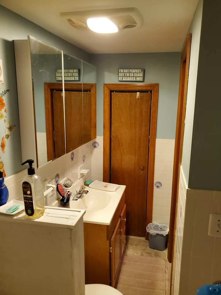 A bathroom with blue walls, a white tiled lower wall, a wooden vanity cabinet, a mirror, and a wooden door.