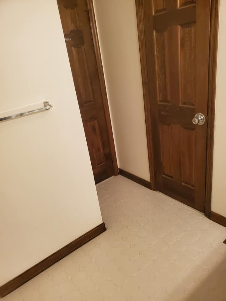 A narrow hallway with two closed wooden doors and a silver towel rack on the white wall.