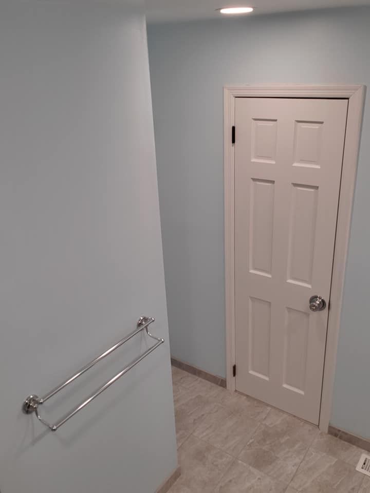 A high-angle view of a hallway with light blue walls, a light-colored tiled floor, a closed white door, and a towel rack.