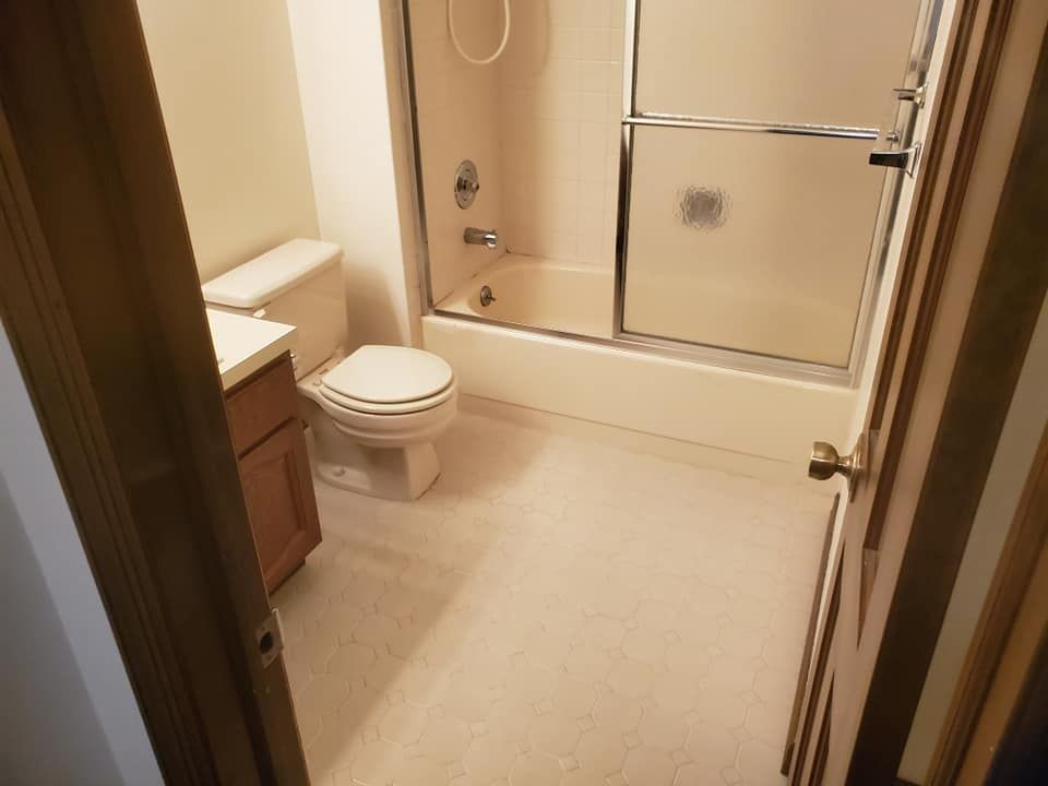 A neutral-toned bathroom featuring a toilet, a wooden vanity with a white countertop, and a shower-tub combination.